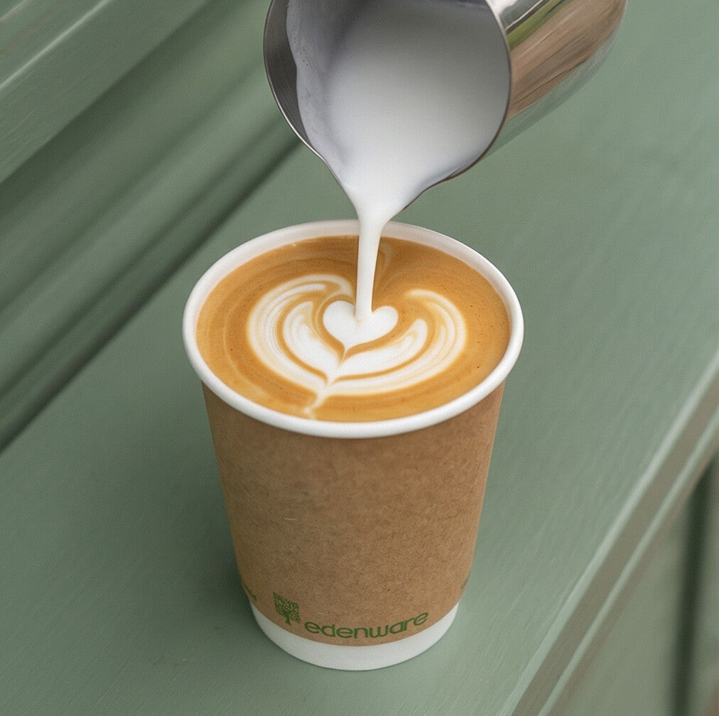 12oz compostable kraft double wall paper cup with latte art being poured from milk jug on green surface