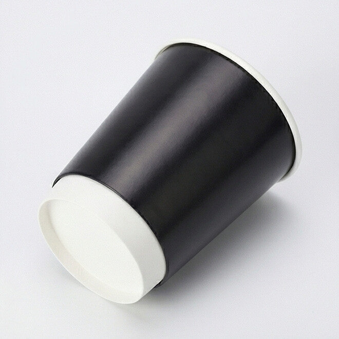 16oz black double wall paper cup tilted to show the white base band and flat base circle, matte black body on light grey