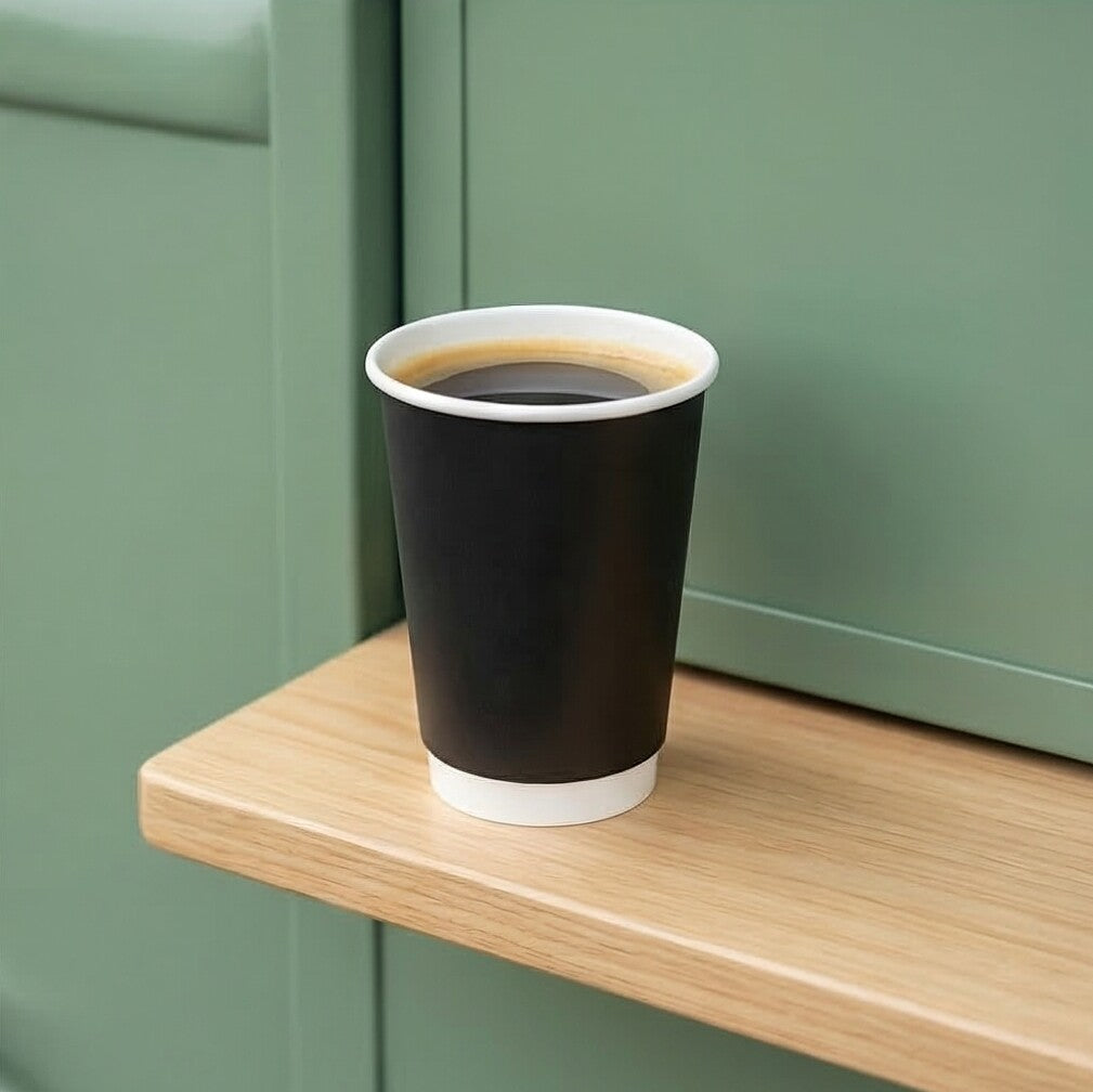16oz Black Double Wall Paper Cup filled with black coffee on a wooden café shelf against sage green cabinetry