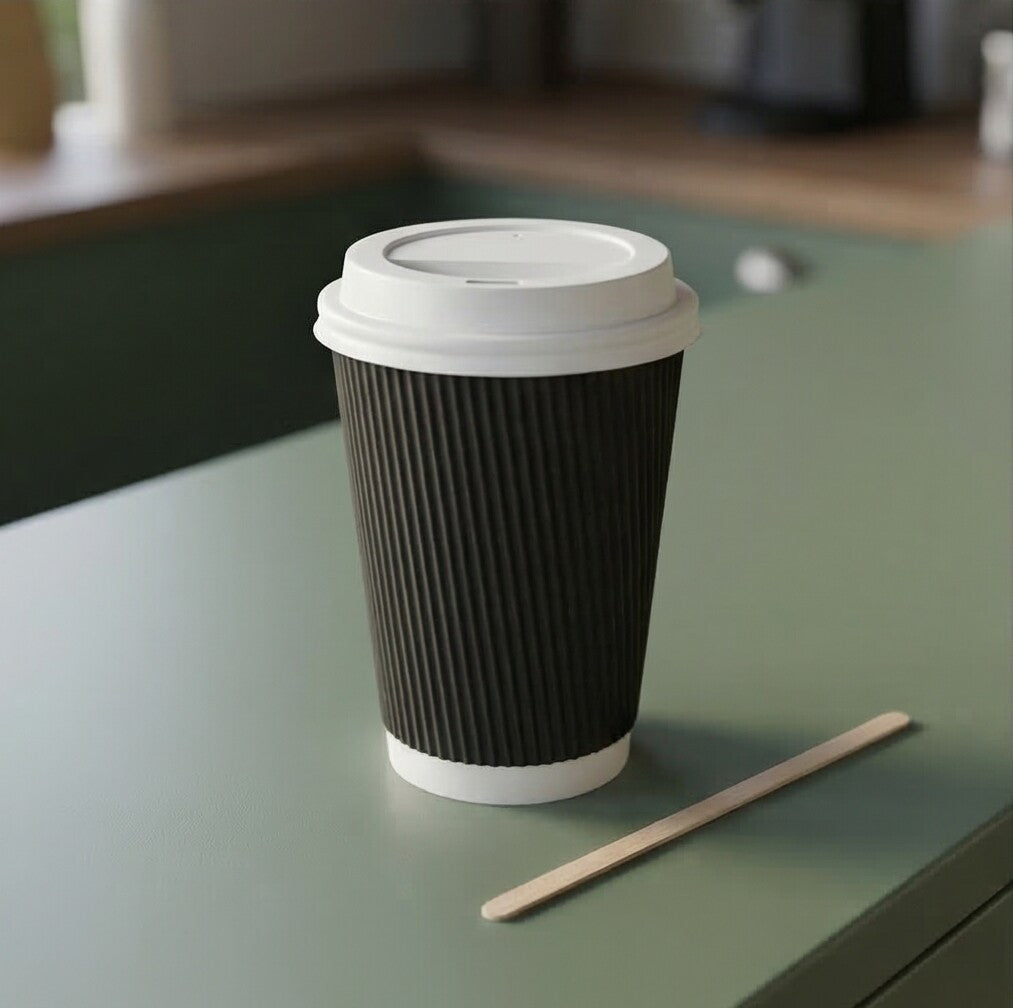 16oz Black Ripple Wall Paper Cup with white lid and wooden stirrer beside on a sage green café counter