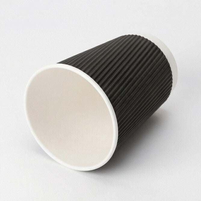 16oz black ripple wall paper cup tipped on its side on light grey, showing the open interior and white base ring