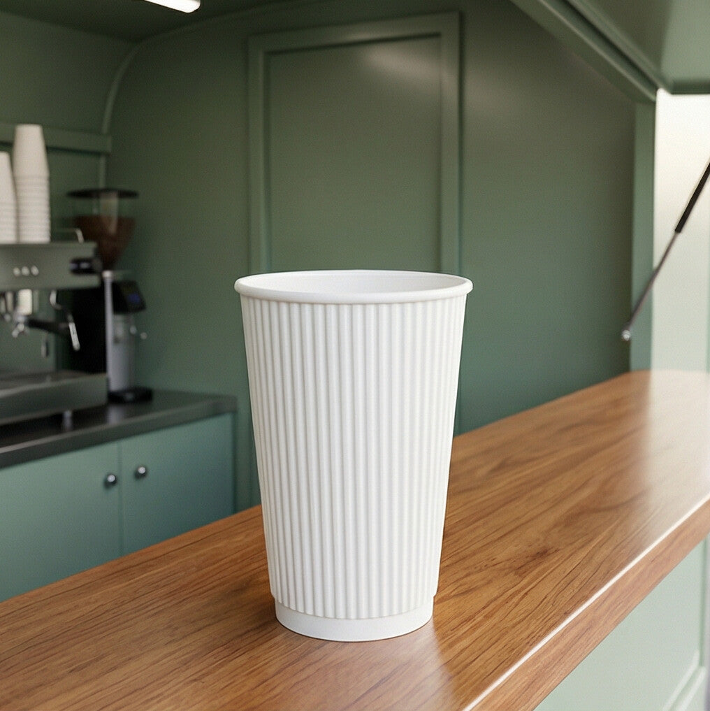 Empty 16oz White Ripple Wall Paper Cup on wooden counter inside a sage green coffee van, espresso machine behind