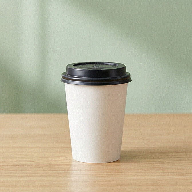 62mm black domed sip-through lid on white paper cup on wooden table with natural light and green background
