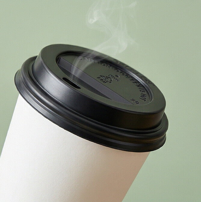 62mm black domed sip-through lid on white paper cup with steam rising on sage green background