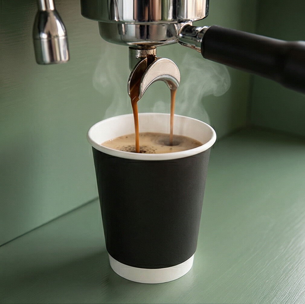 Double espresso being pulled directly from a portafilter into a black 8oz double wall paper cup on a sage green counter