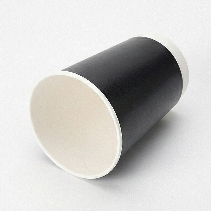 Black double wall paper cup tipped on its side on a light grey background, showing the white interior and flat base circle