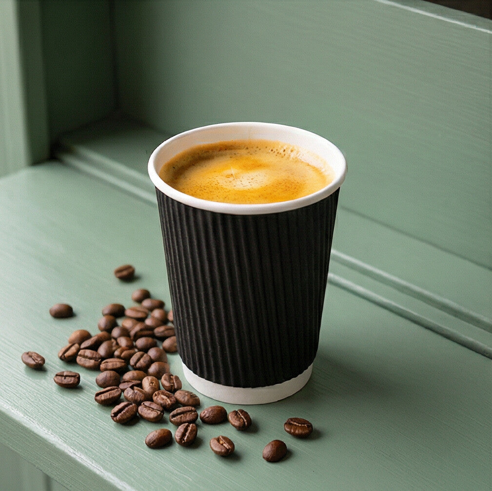 8oz Black Ripple Wall Paper Cup filled with espresso on a sage green surface, scattered coffee beans beside