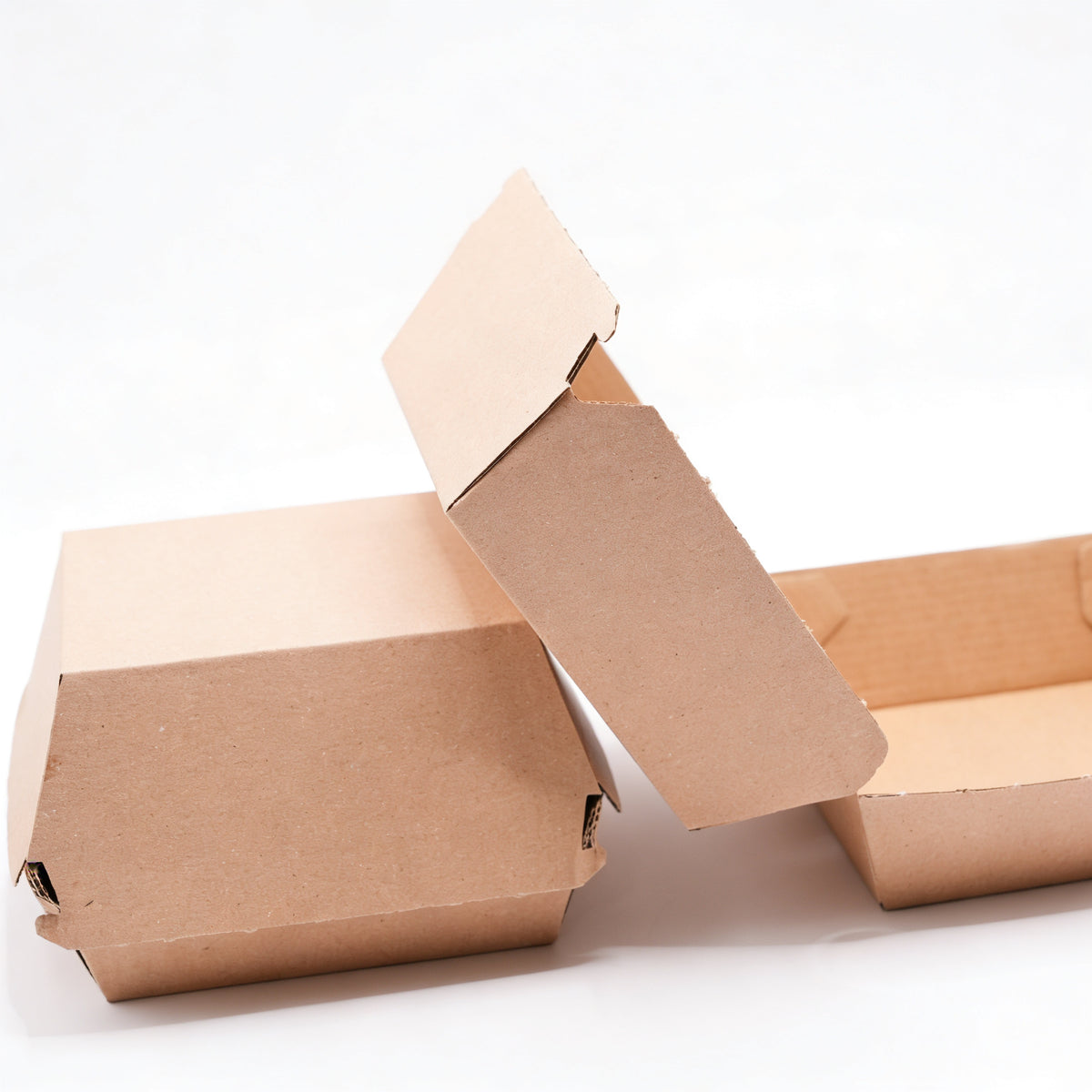 Small corrugated burger boxes styled group view showing one closed box, one open with lid raised, and one flat base, natural kraft brown corrugated construction on white background
